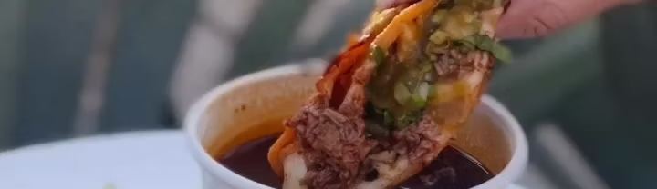 A taco being dipped into a cup of consomé.
